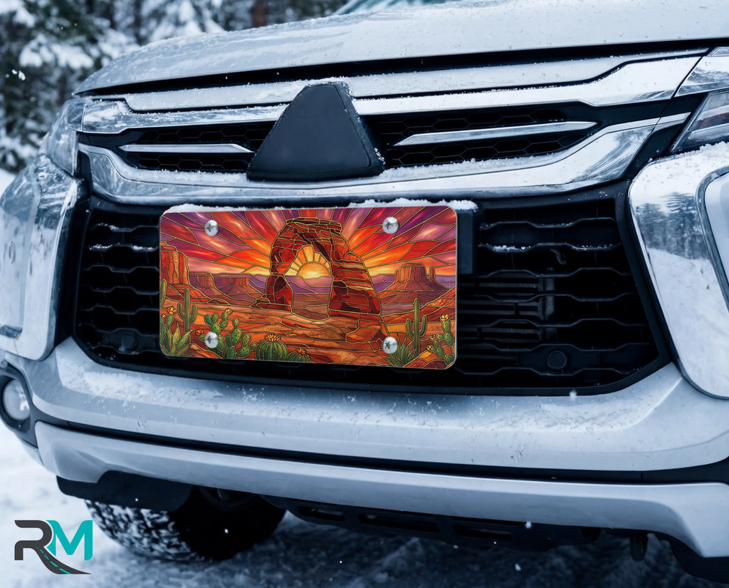 desert arch sunset vanity plate on car in snowy setting — warm amber sandstone arch cactus sunset design