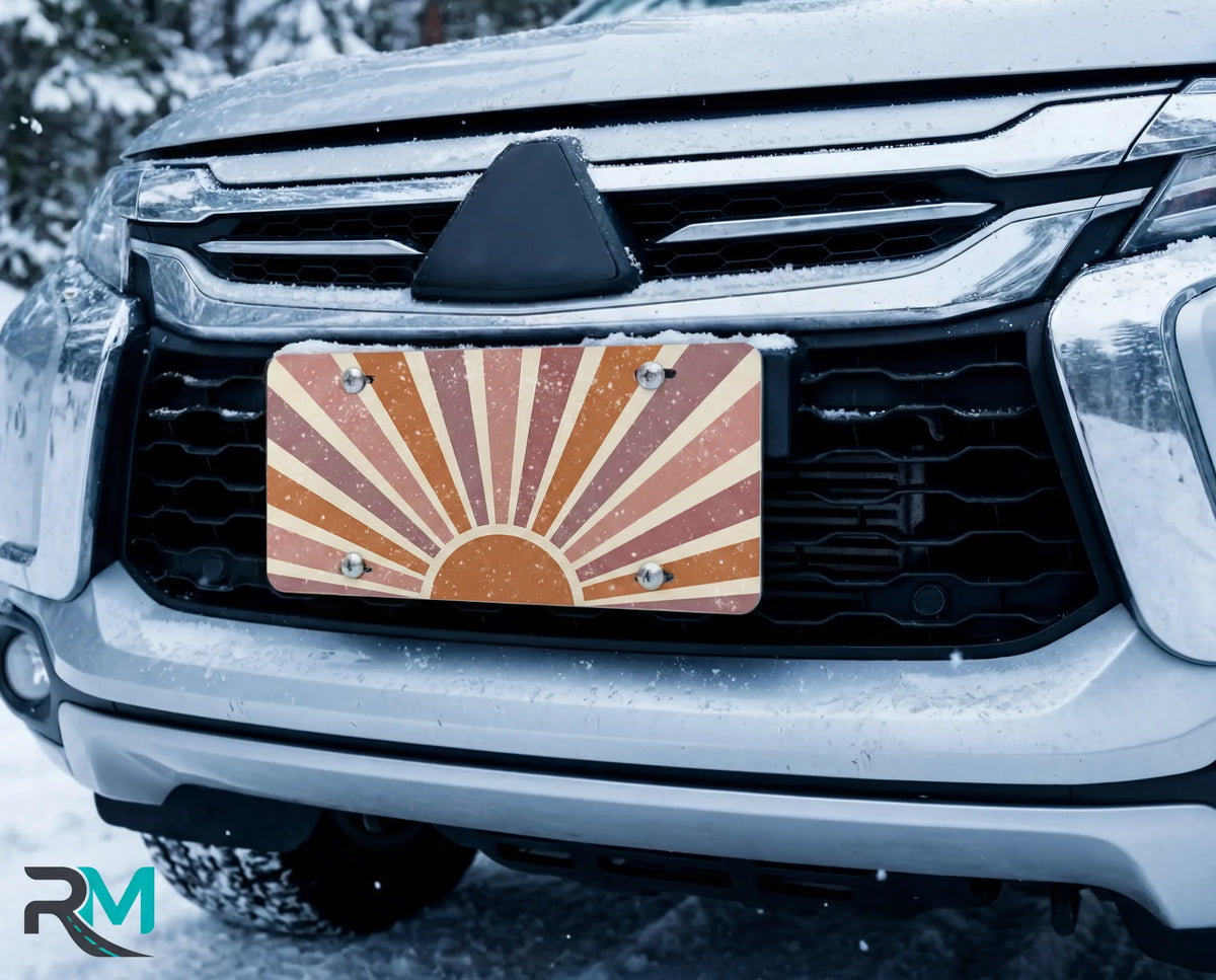 terracotta sunrise license plate on car in snowy setting — muted boho sunburst design